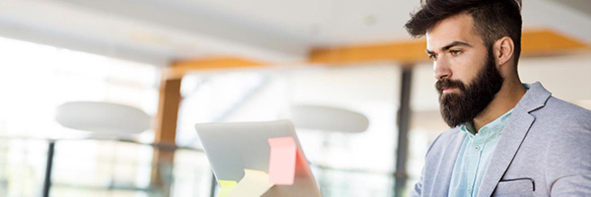 Tarjetas para Autónomos y Comercios - Joven autónomo con traje y barba trabajando frente a su portátil en su negocio buscando tarjetas para su negocio Tarjetas para Autónomos y Comercios - Joven autónomo con traje y barba trabajando frente a su portátil en su negocio buscando tarjetas para su negocio